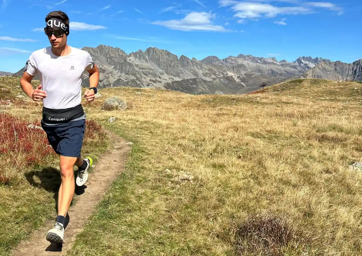 Trailrunner mit schwarzem Conquer. Laufgürtel und Conquer. Laufflasche 500 ml läuft in schönem Alpenpanorama